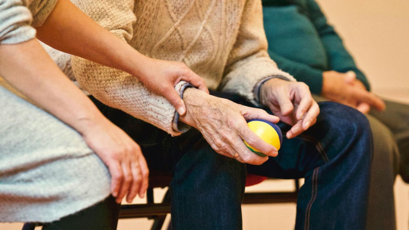 An old man holding a ball while a nurse rests her hand on his arm