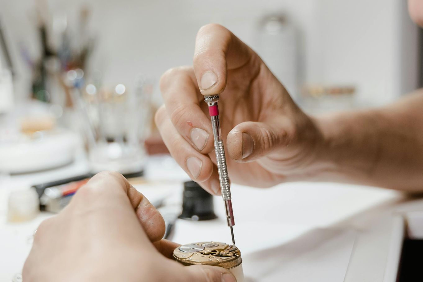 Two disembodied hands working on a watch in a tidy workshop